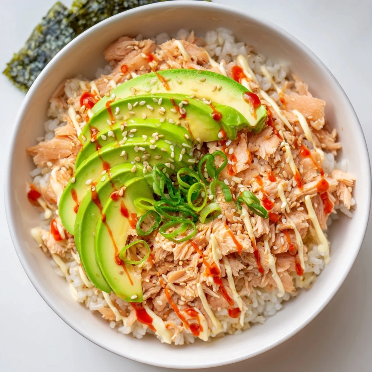 Freshly prepared Emily Mariko Salmon Rice Bowl topped with creamy avocado slices and drizzled with spicy mayo.