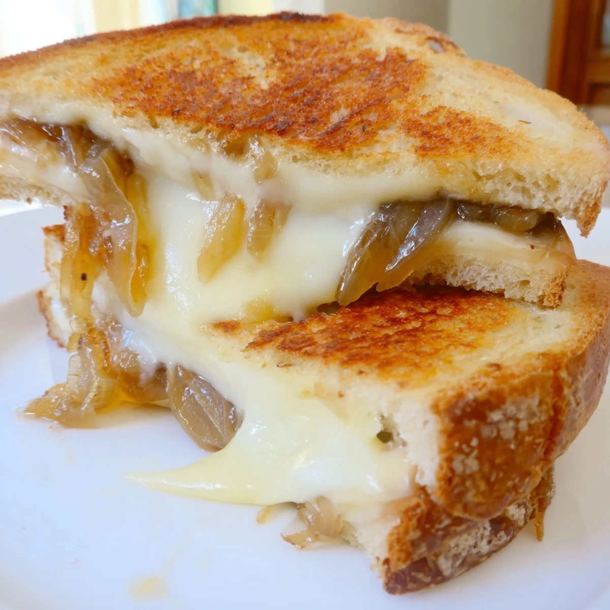 Golden-brown Caramelized Onion Grilled Cheese slices on a plate, with melty sharp white cheddar oozing from between buttery sourdough.