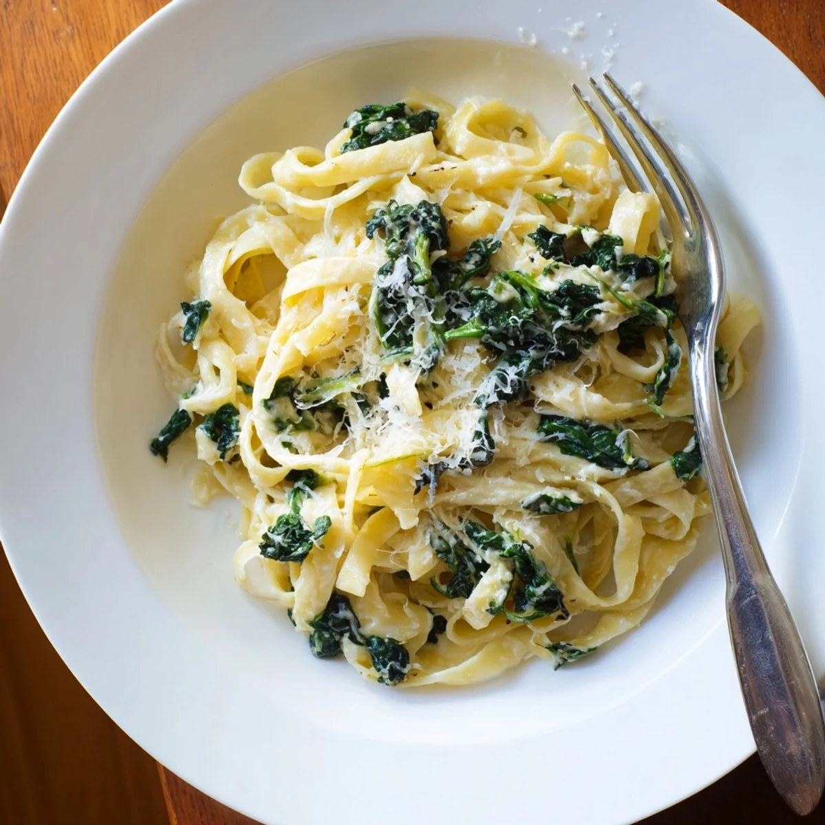 A close-up of creamy garlic spinach pasta twirled on a fork, showcasing wilted spinach and rich Parmesan sauce.  