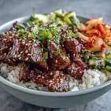 Close-up of a Korean Beef Bowl, showing seasoned beef, chopped kimchi, and sliced radish over rice, garnished with green onions and sesame seeds.