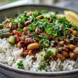 A close-up of vegetarian Hoppin' John served over fluffy rice, garnished with fresh parsley and sliced green onions.