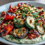 Colorful array of charred zucchini, red onion, and cherry tomatoes arranged on a platter with smooth, homemade hummus—perfect for picnics and barbecues.  