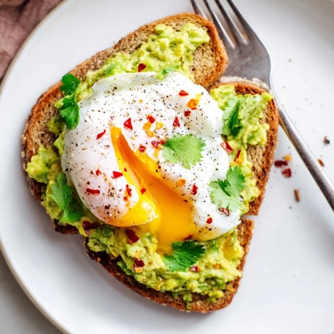 Sliced avocado toast topped with a poached egg and chili flakes enhances breakfast flavor.  