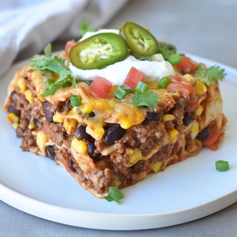 A steaming skillet of taco lasagna with melted cheese, ready for the oven.
