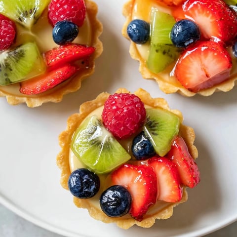 Mini fruit tartlets arranged in a circle, showcasing vibrant berries and a sweet, creamy filling within golden crusts.