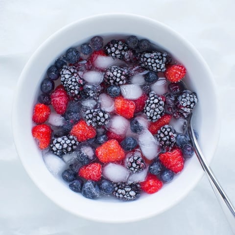 This vibrant Nature's Cereal Bowl showcases fresh blueberries, raspberries, and strawberries glistening over ice in a chilled coconut water broth.