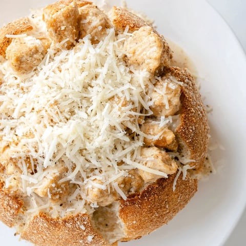 Golden, baked bread bowl overflowing with creamy chicken Alfredo and topped with fresh parsley and grated Parmesan.