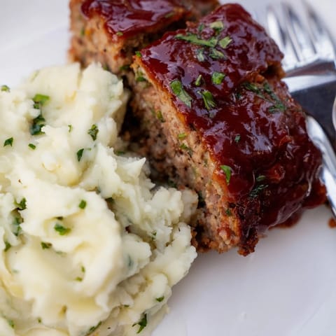 Tender meatloaf smothered in ketchup glaze alongside fluffy mashed potatoes and chives.  