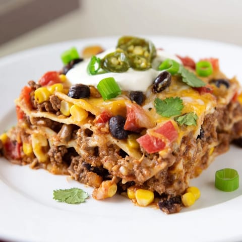 This baked taco lasagna is layered with seasoned beef, veggies, and shredded cheese.