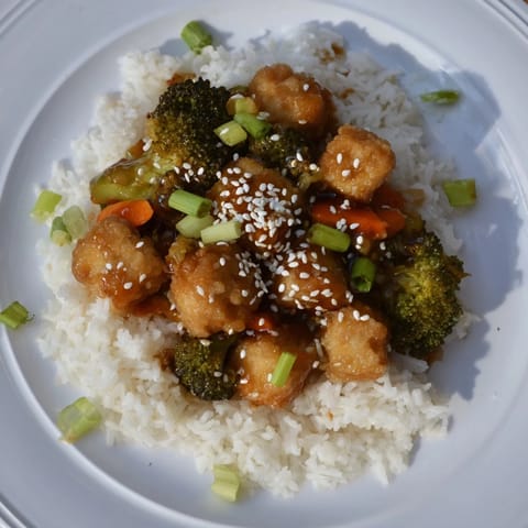 A close-up image shows steaming sesame tofu & broccoli with fluffy rice and sprinkled sesame seeds.
