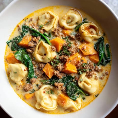 Rustic close-up of creamy sausage tortellini soup, highlighting the richness of the Italian-American flavors.