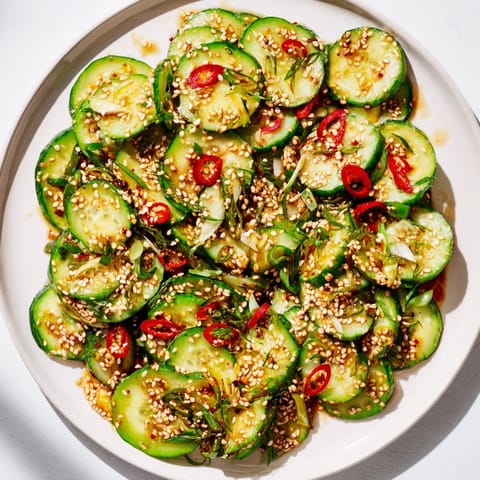 Close-up of a refreshing Tangy Shaken Asian-Style Cucumber Salad, glistening with a savory dressing and sesame seeds.
