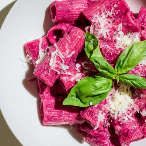 Warm pink pasta with beet cream served in a shallow bowl, showcasing its rich color and creamy texture for a stunning vegetarian main dish.