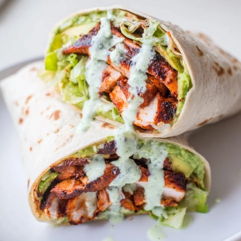 A close-up of Smoky Chipotle Chicken Wrap sliced on a wooden board, revealing layers of tender chicken, creamy avocado, and crisp lettuce.  