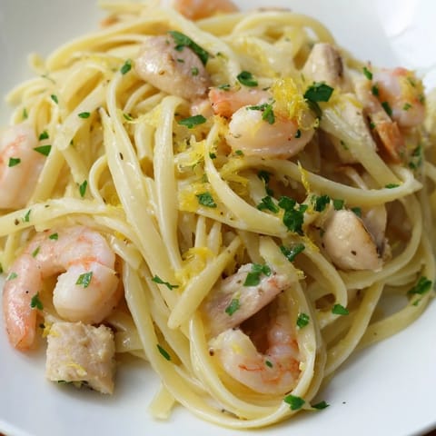 Plated Lemon Garlic Shrimp & Chicken Pasta garnished with fresh parsley and lemon wedges, served alongside a crisp green salad for a complete meal.