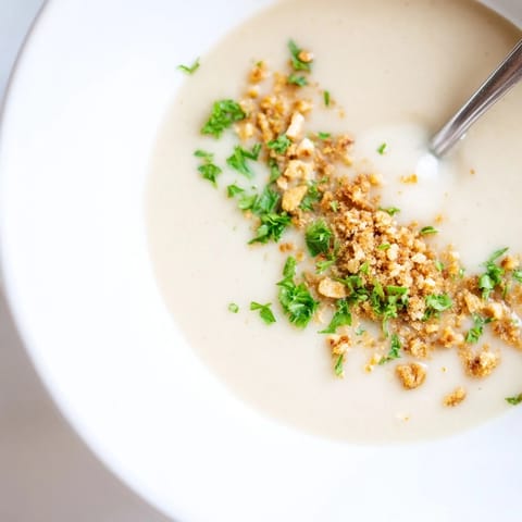 A close-up of velvety celeriac soup topped with golden hazelnut crumble and fresh parsley, served in a rustic bowl.