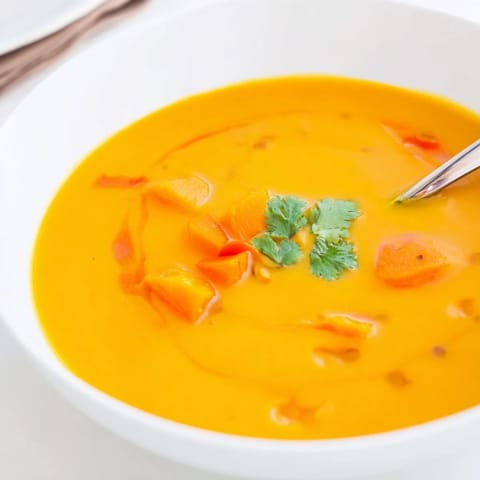 Creamy butternut squash and lentil soup in a rustic bowl, garnished with fresh cilantro and a lemon wedge beside crusty gluten-free bread for dipping.