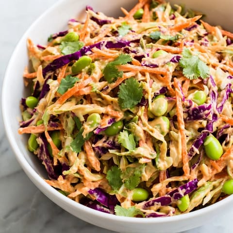Tossing the Crunchy Thai Peanut Salad with creamy peanut dressing, garnished with scallions, cilantro, and sesame seeds, perfect for a refreshing vegan meal.