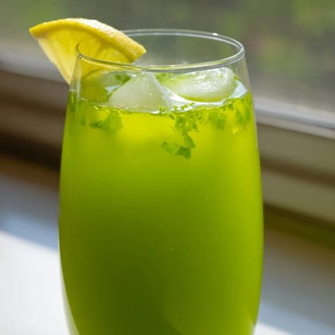 A tall glass of vibrant Celery Ginger Lemon Juice garnished with fresh mint, set on a wooden table for a refreshing morning beverage.