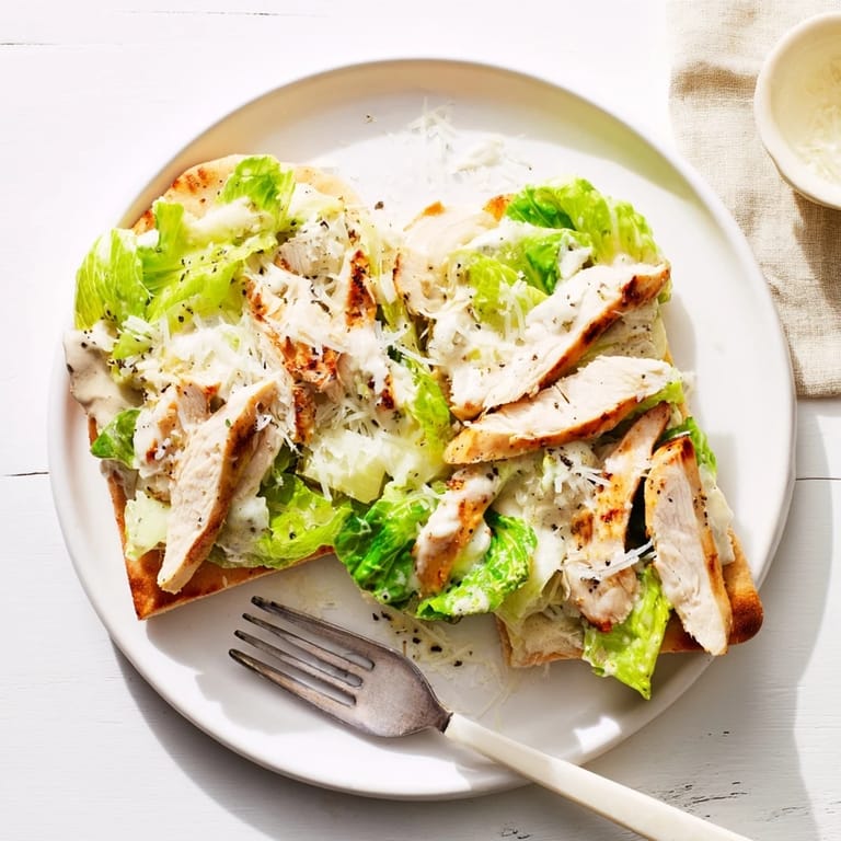 Slices of juicy grilled chicken and fresh romaine garnish a warm, golden flatbread drizzled with tangy Caesar dressing and parmesan.  
