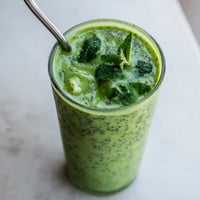 Two vibrant glasses of Green Detox Smoothie garnished with fresh mint and a lemon wedge on a bright kitchen counter.  